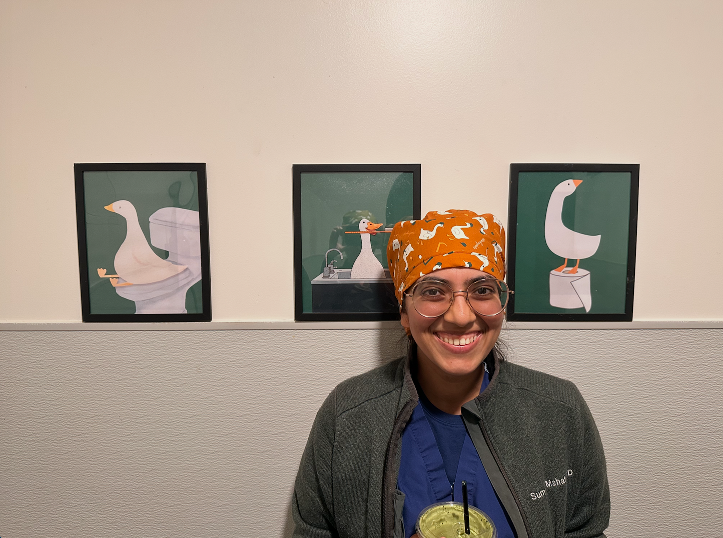 Person wearing an orange scrub cap with a goose design in front of three framed pictures of geese.