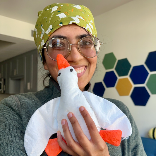 Person wearing a green patterned scrub cap holding a white plush goose.